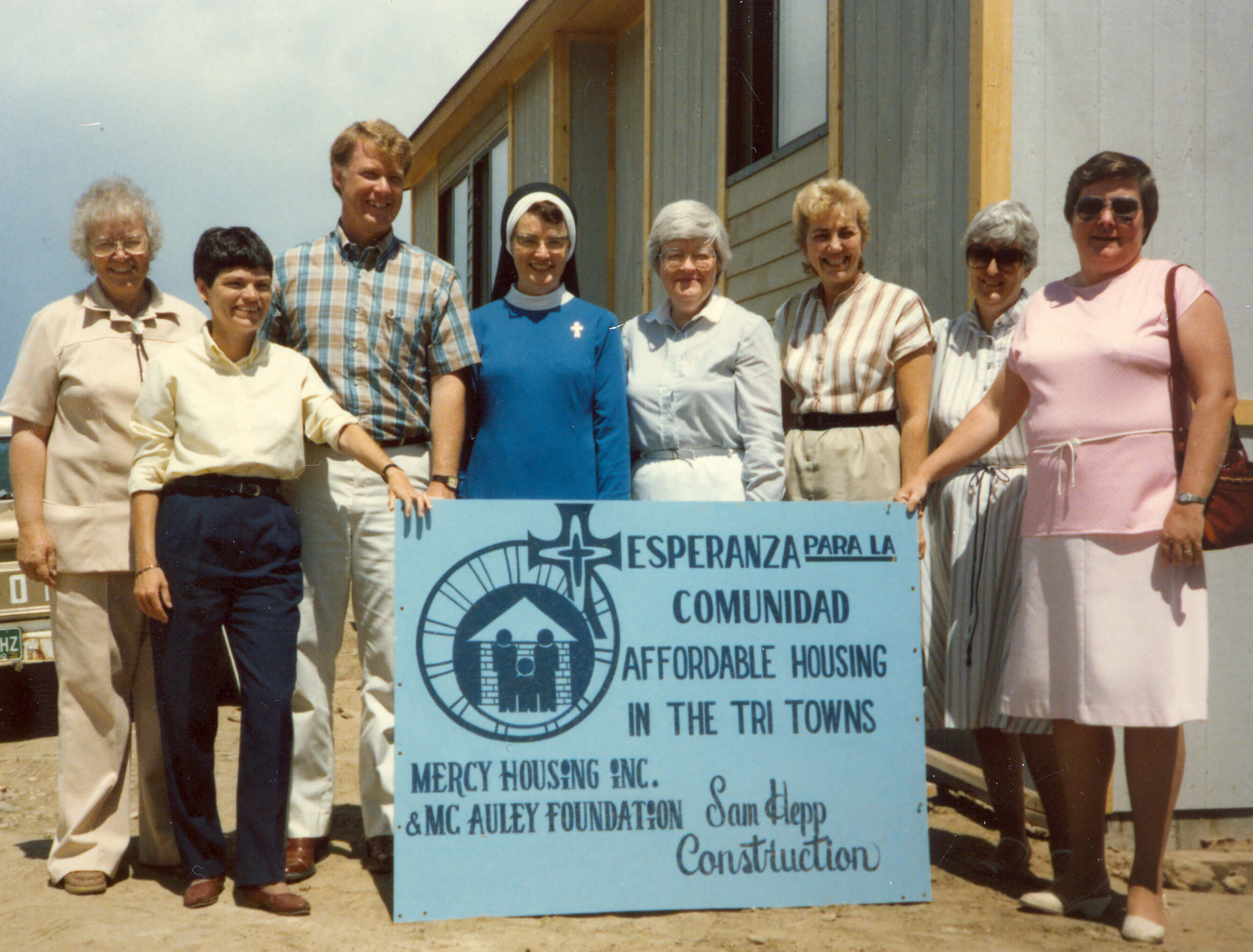 Group of people holding up sign that reads 'Ezperanza de la comunidad, affordable housing in the tritowns. Mercy housing and Mac Auley foundation.'