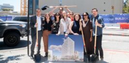 Staff and partners stand at the construction site holding a rendering of what the finished building will look like