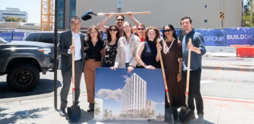 Staff and partners stand at the construction site holding a rendering of what the finished building will look like