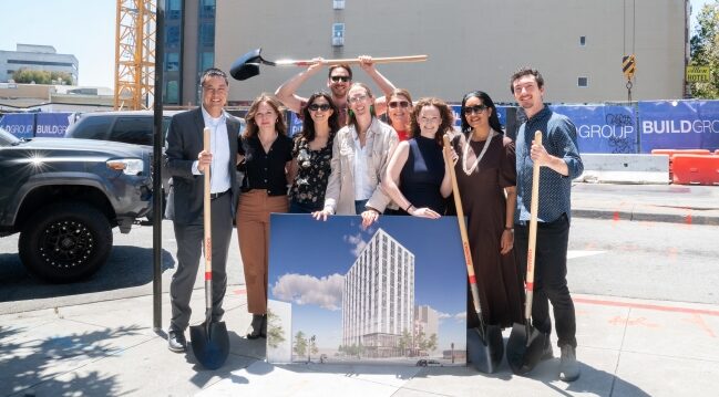 Staff and partners stand at the construction site holding a rendering of what the finished building will look like